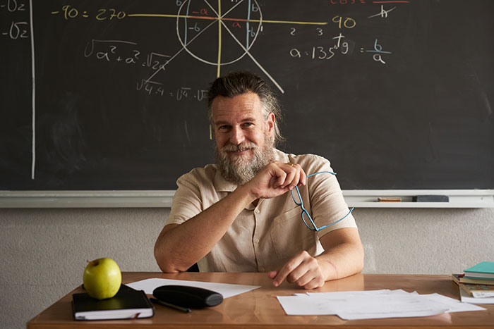 Bearded man in front of a chalkboard with math formulas, holding glasses, illustrating creepy parts of their jobs concept.