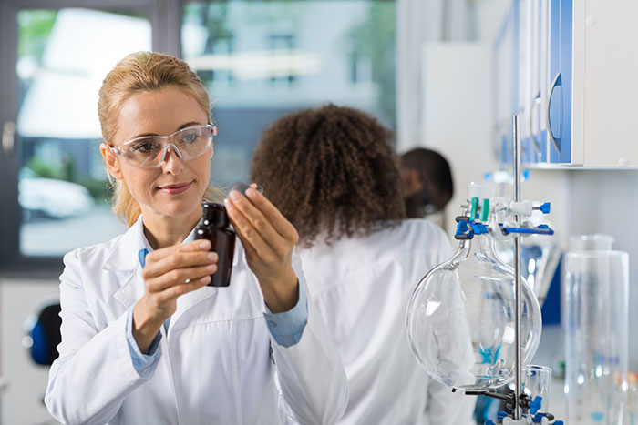 Female scientist wearing safety glasses examines a bottle in a lab highlighting creepy parts of their jobs.