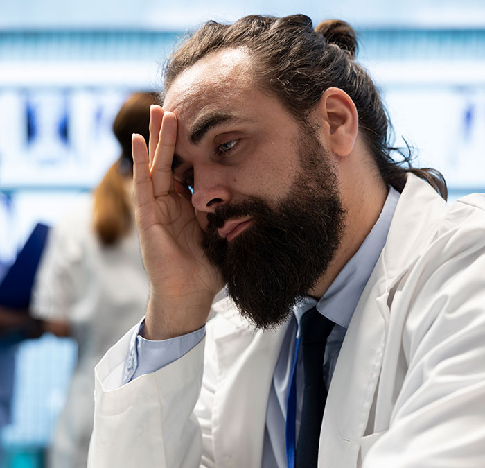 Stressed male worker with beard and hair bun in a white coat, showing the creepiest parts of their jobs experience.