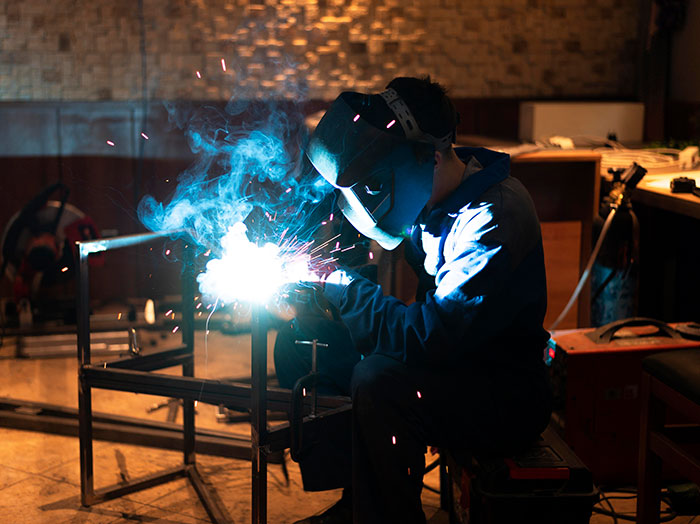Worker welding metal sparks flying in a dim workshop illustrating the creepiest parts of jobs revealed by 92 workers.