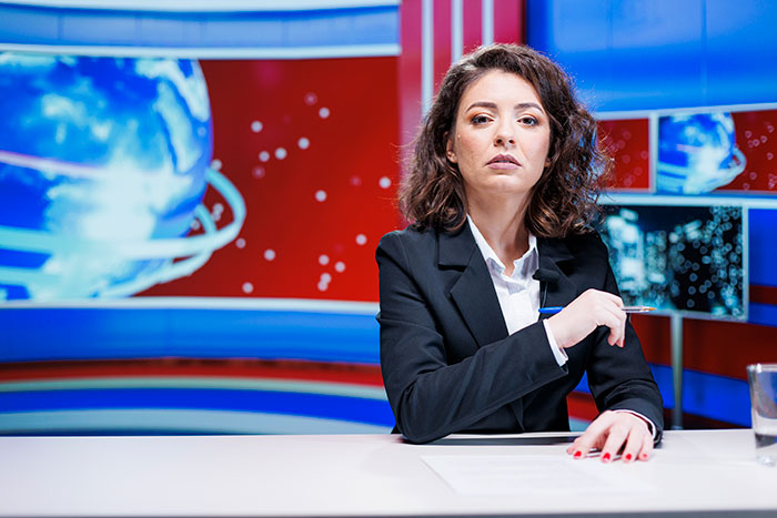 Female news anchor in a black suit reporting on the creepiest parts of jobs including driving over two humans career risks.