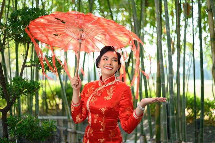 Woman in traditional attire holding a red parasol outdoors reflecting cultural attire swap and appropriation debate.
