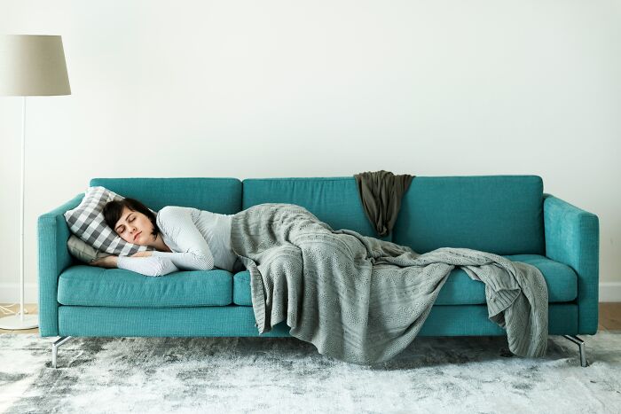 Woman resting on a sofa covered with a blanket, illustrating creative ways to avoid babysitting duties at home.