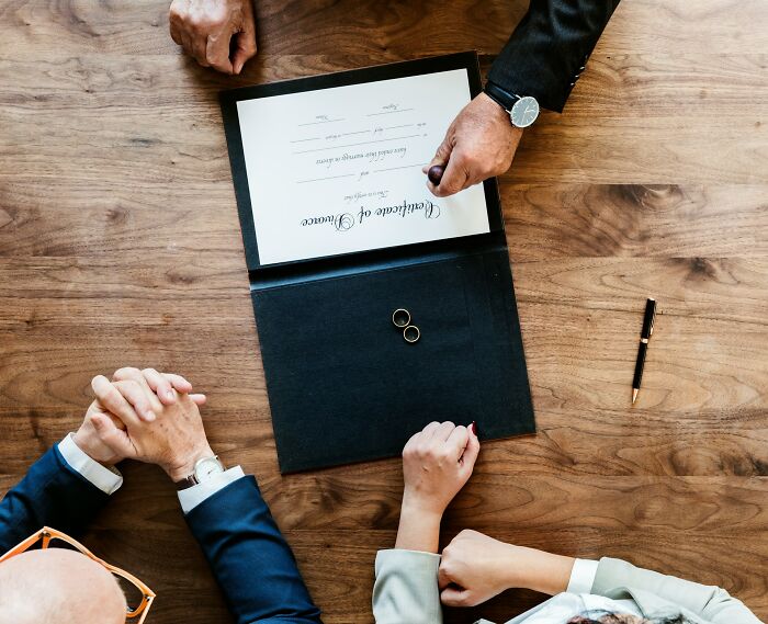 Couple signing a marriage certificate with two wedding rings on the table symbolizing unexpected wedding registry items.
