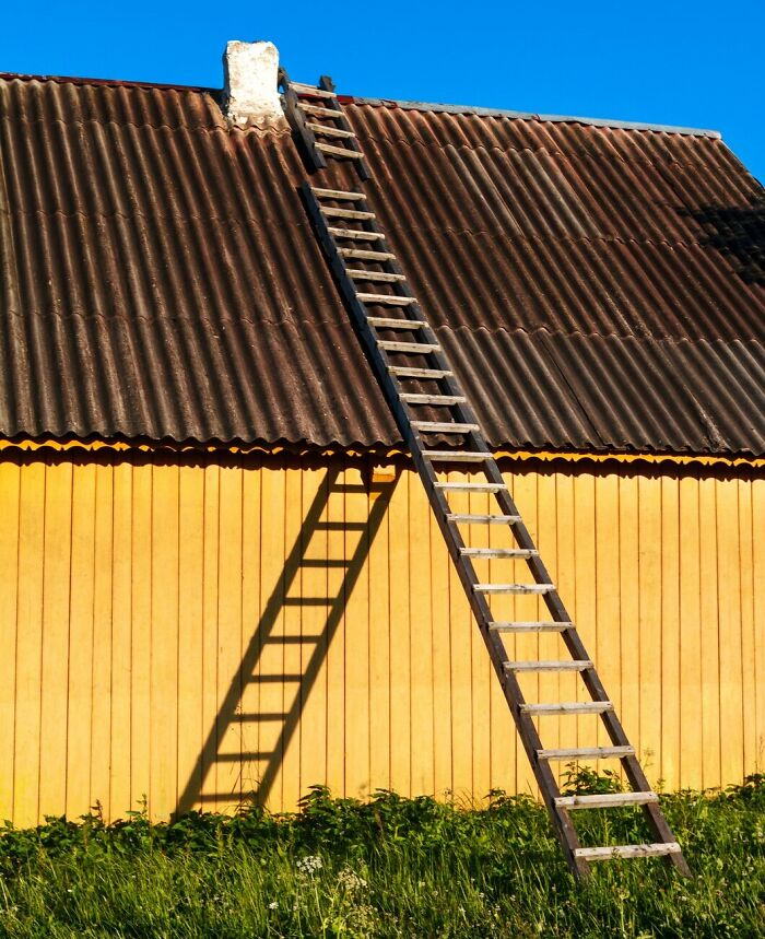 Wooden ladder leaning against a yellow house roof under clear blue sky representing skipped work day reasons