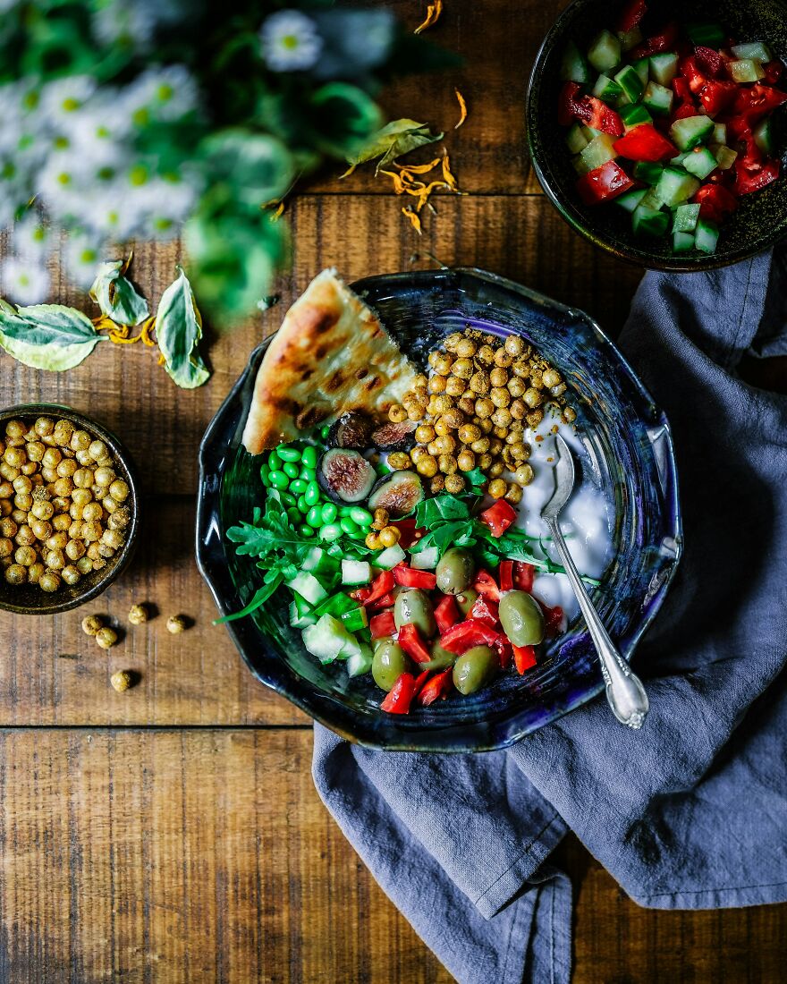 A bowl of fresh vegetables, olives, chickpeas, yogurt, and bread on a wooden table, promoting weight loss foods.
