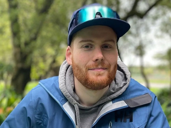Young man with red beard wearing a blue jacket and cap outdoors, symbolizing Good Samaritan protecting mom and children.