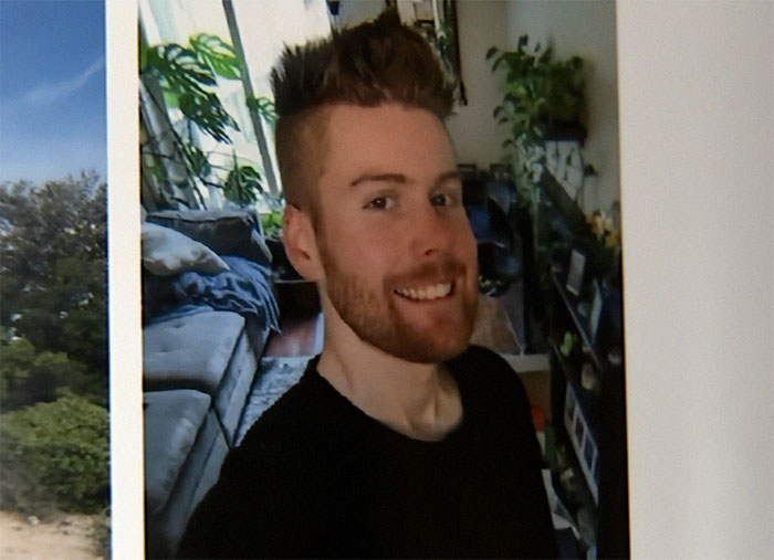 Smiling man with a beard in a black shirt inside a cozy living room, symbolizing good Samaritan protecting helpless mom and children.