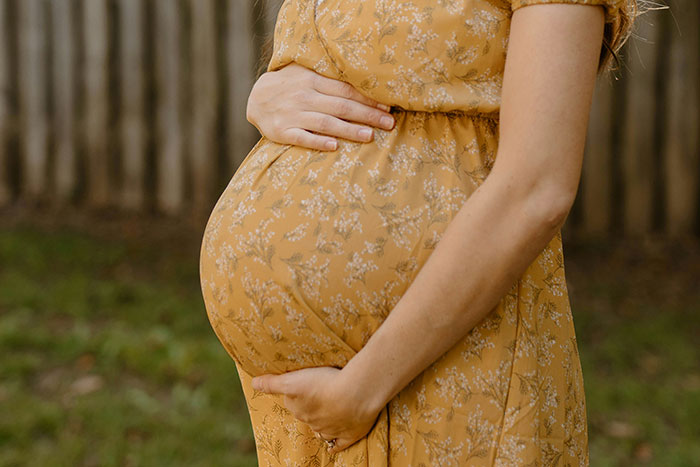 Pregnant woman in a yellow floral dress holding belly outdoors, representing dad&rsquo;s difficult decision to call CPS on teen daughter.
