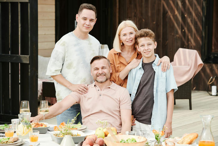 Family dinner scene with smiling dad, mom, and stepsiblings outdoors, highlighting family dynamics and rejection.