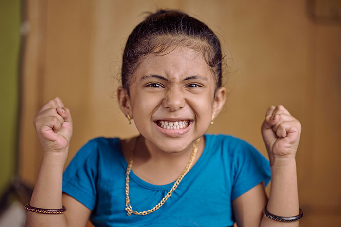 Angry young girl clenching fists, reflecting frustration over stepdad suggesting punishment for using native language.