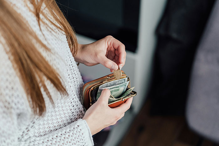Woman holding wallet with cash and coin, symbolizing refusal to join Christmas gift trip if siblings pay flight.