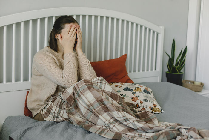 A distressed woman sitting on bed covering her face, illustrating creepy and disturbing things police officers saw at homes.