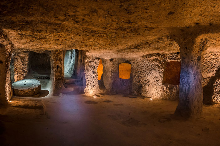 Ancient mysterious underground city 18 stories deep with carved stone pillars and rooms illuminated by soft lights.