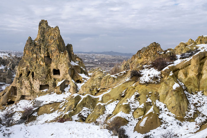 Ancient underground city carved into rocky terrain covered with snow, showcasing mysterious multi-level hidden dwellings.