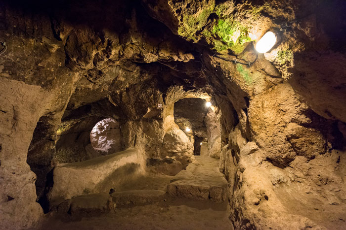 Underground city tunnels with carved rock walls illuminated by lights, showcasing mysterious 18-story deep ancient passageways.