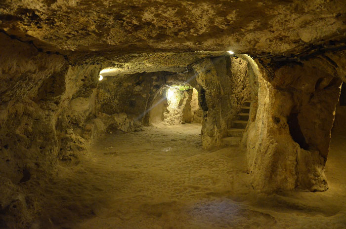 Dimly lit passage inside a mysterious underground city carved from rock, showcasing tunnels and stairways deep below the surface.