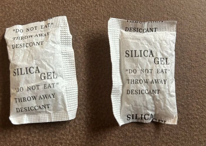 Two silica gel packets on a brown surface, illustrating one of the totally safe things people freak out about online.