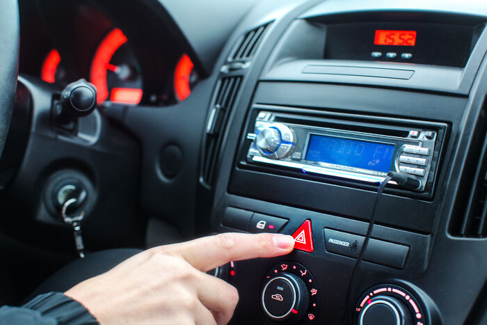 Person pressing hazard button inside a car dashboard with illuminated controls, linked to terrifying things people swear they've seen.