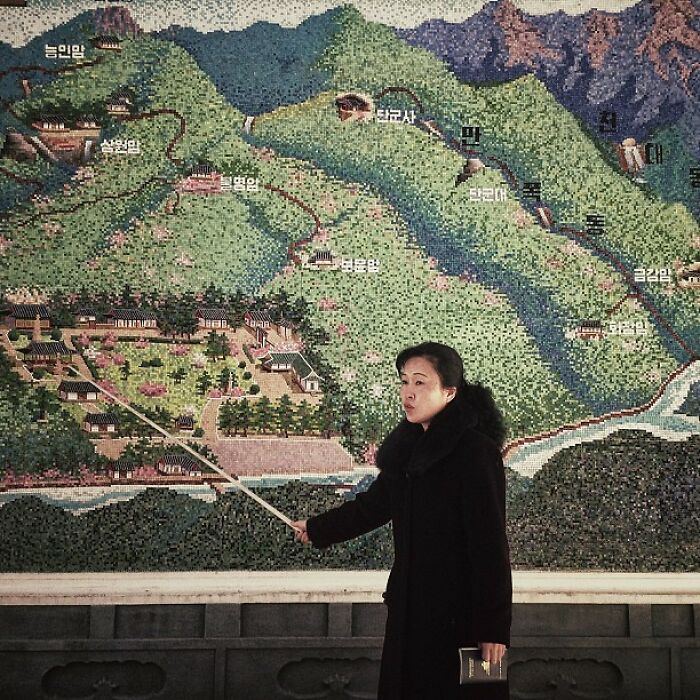 A woman in black coat pointing at a large detailed map on the wall, capturing iconic moments in history.
