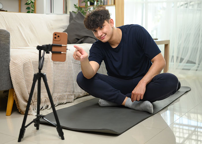Young man sitting on a yoga mat at home, filming a video about disgusting things people discovered about their friends.