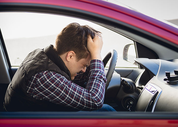 Man sitting in a red car, holding his head in frustration, reflecting on disgusting things discovered about friends.