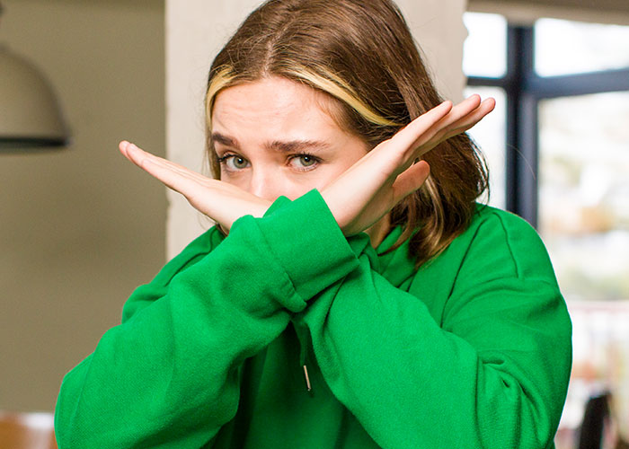 Young woman in a green hoodie crossing arms in a defensive pose, reflecting disgust and distrust about friendships discovered.