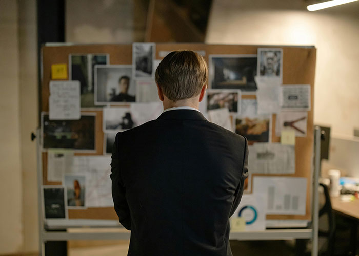 Man in suit examining a board with notes and photos, reflecting on disgusting things discovered about friends.