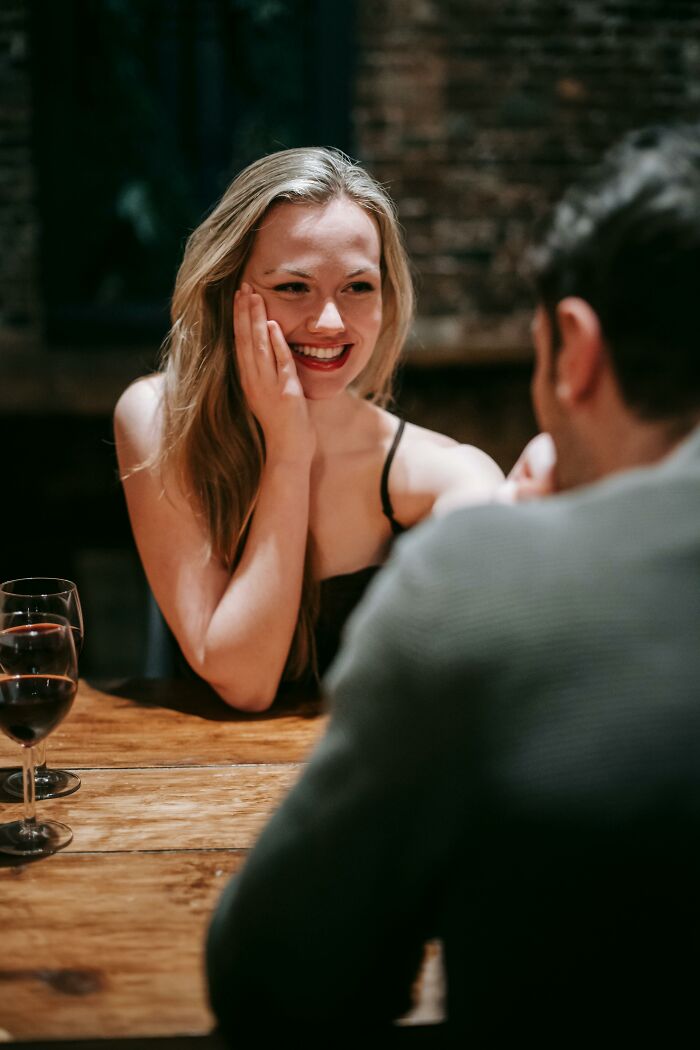 A woman smiling and talking with a man over wine at a wooden table, illustrating people who found out disgusting secrets.