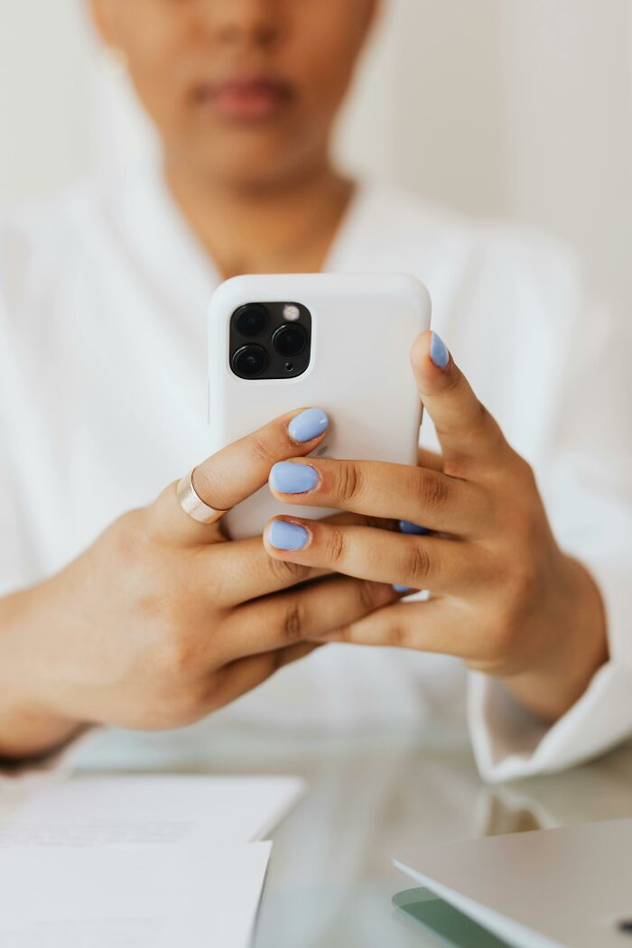 Person with blue nail polish holding smartphone, discovering something disgusting about a friend on their device.