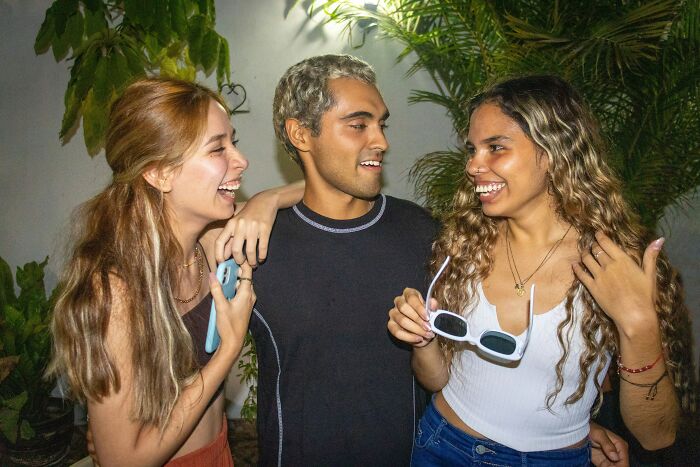 Three friends laughing and talking outside at night, capturing a moment of friendship before hidden truths emerge.