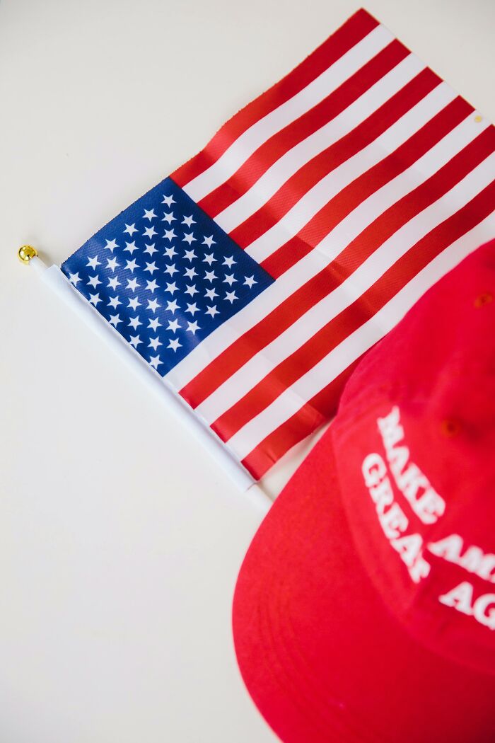 Small American flag next to a red Make America Great Again hat on a white surface symbolizing friendship and trust.