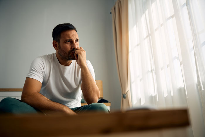Man sitting pensively by a window, portraying the emotional impact of in-laws' concerns about weight and divorce.