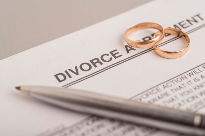 Divorce agreement form with two gold wedding rings and a silver pen symbolizing in-laws' misunderstanding about weight.