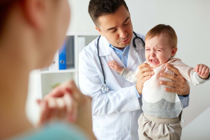 Doctor examining a crying baby held by a parent, illustrating disturbing facts that don’t help to sleep at night.