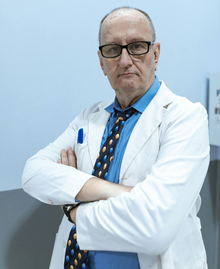 Man in white coat and glasses with arms crossed, representing doctor receiving calls meant for another person.