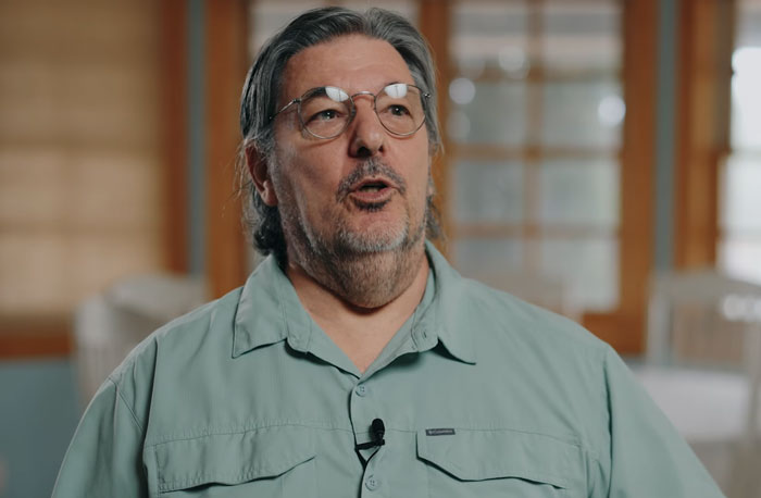 Middle-aged man with glasses speaking indoors in a casual setting, discussing loyal dog confronting raging bull story.