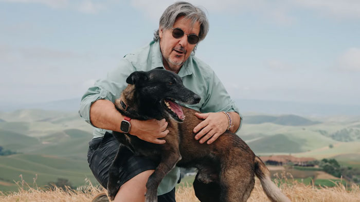 Man kneels outdoors hugging loyal dog with a hero&rsquo;s smile after confronting a raging bull to protect owners.