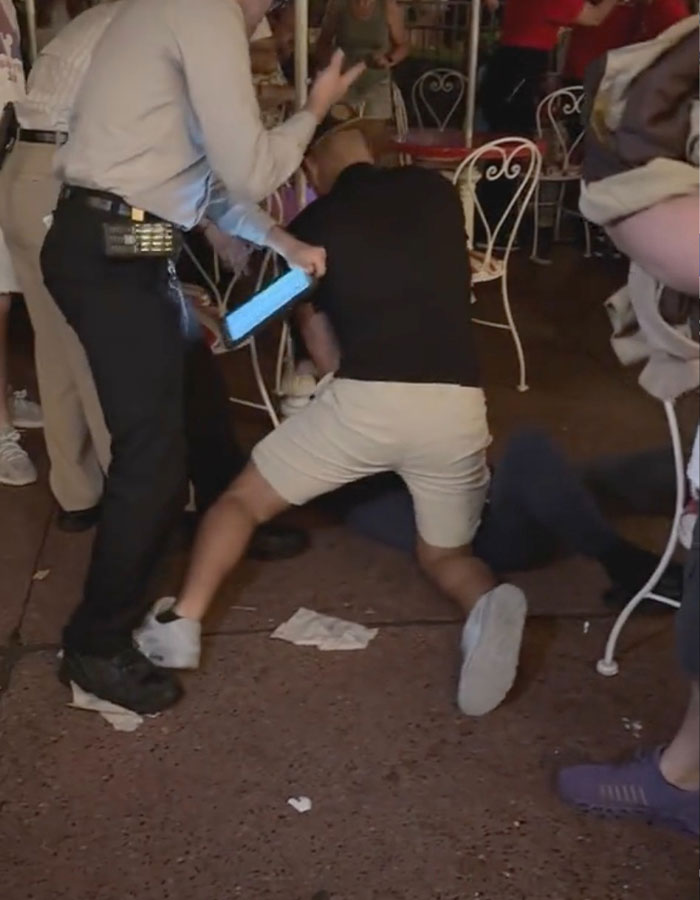Man in black shirt crouching over another person during a violent Disney World incident with bystanders nearby.