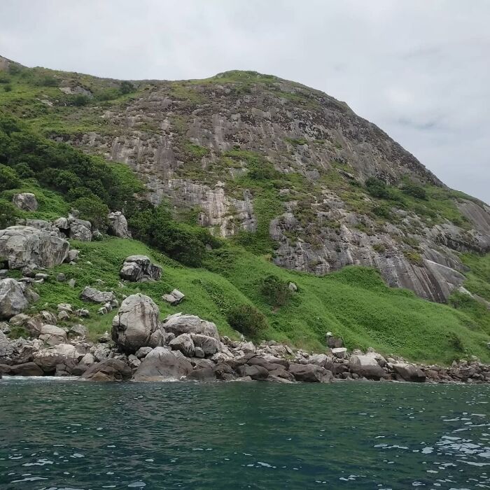 Rocky hillside covered with patches of greenery rising above a calm body of water in an abandoned place setting.