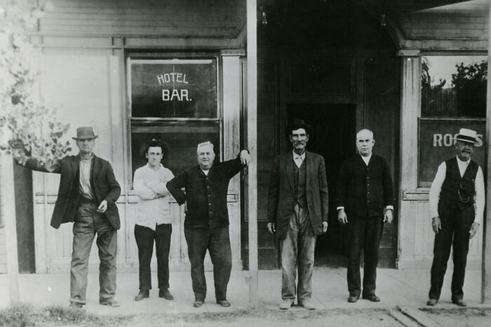 Group of six men standing outside an early hotel and bar, capturing a historic moment in the birth of Vegas.