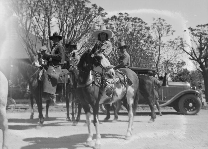 Early Las Vegas scene with cowboys on horseback and a vintage car, showcasing historic life during the birth of Vegas era.