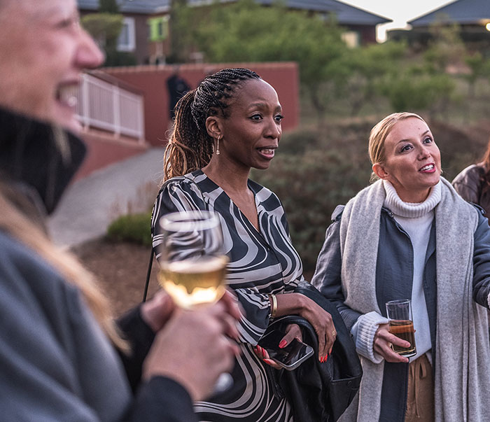 Three women socializing outdoors at dusk, holding drinks, discussing Prince Harry and Sentebale scandal findings. - 8