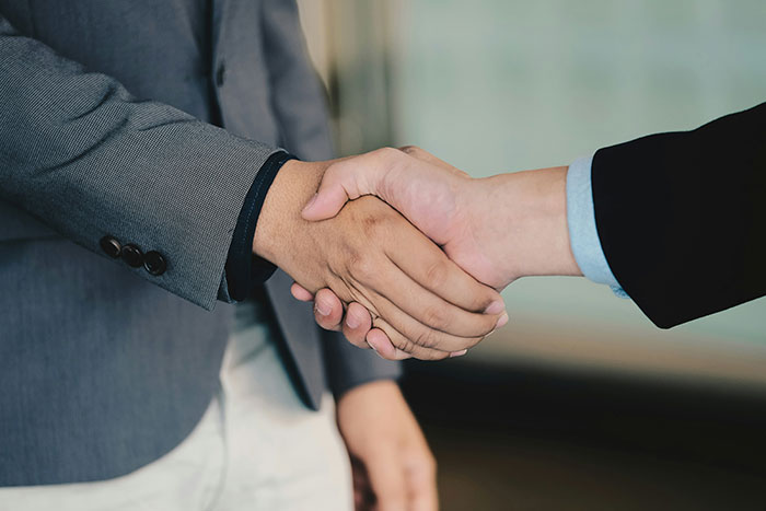 Two neighbors shaking hands in a suit, symbolizing resolution after a driveway dispute and property conflict.