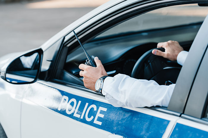 Police officer in patrol car holding a radio, relating to neighbors fight over driveway and property disputes.