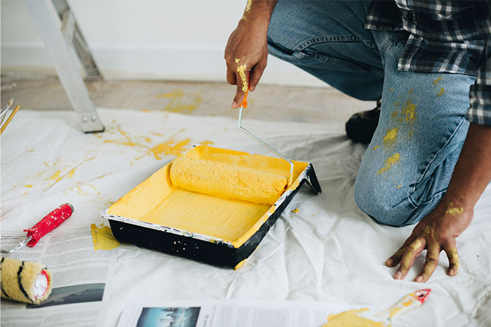 Person kneeling with paint roller covered in yellow paint, illustrating bizarre reasons for divorce discussions.