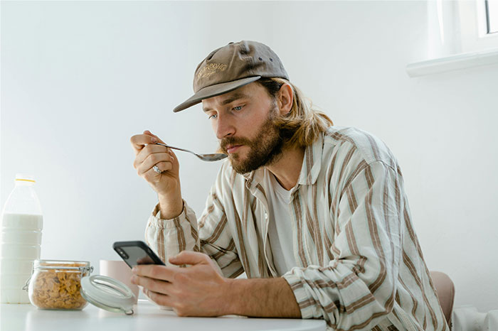Man in casual clothes eating breakfast while checking phone, illustrating bizarre reasons why someone wanted a divorce concept.