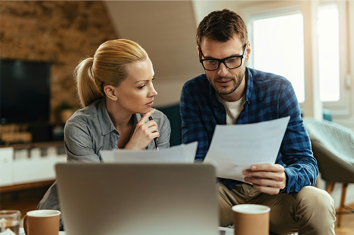 Couple reviewing documents at home, discussing bizarre reasons for divorce while sitting near laptop and coffee cups.