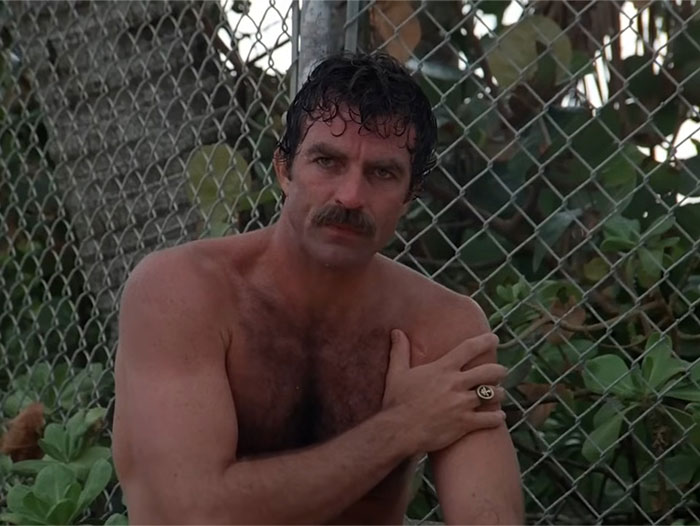 Man with mustache and wet hair sitting shirtless near a chain-link fence, illustrating bizarre reasons for divorce.