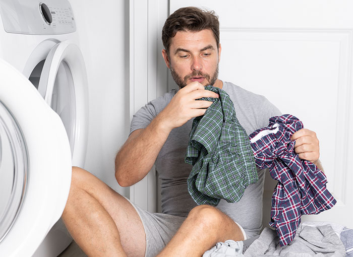 Man sitting by washing machine smelling clothes, illustrating bizarre reasons why someone wanted a divorce concept.
